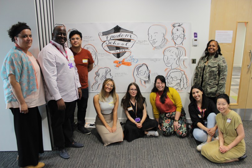 A racially diverse group of participants stands in front of an illustrated banner reading Freedom School. Photo: Thomas Higgins.